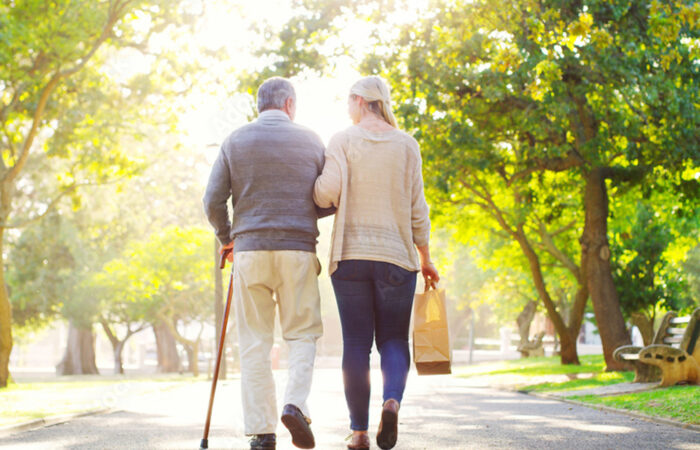 An elderly man links arm with a women and goes on a walk with a bag of groceries